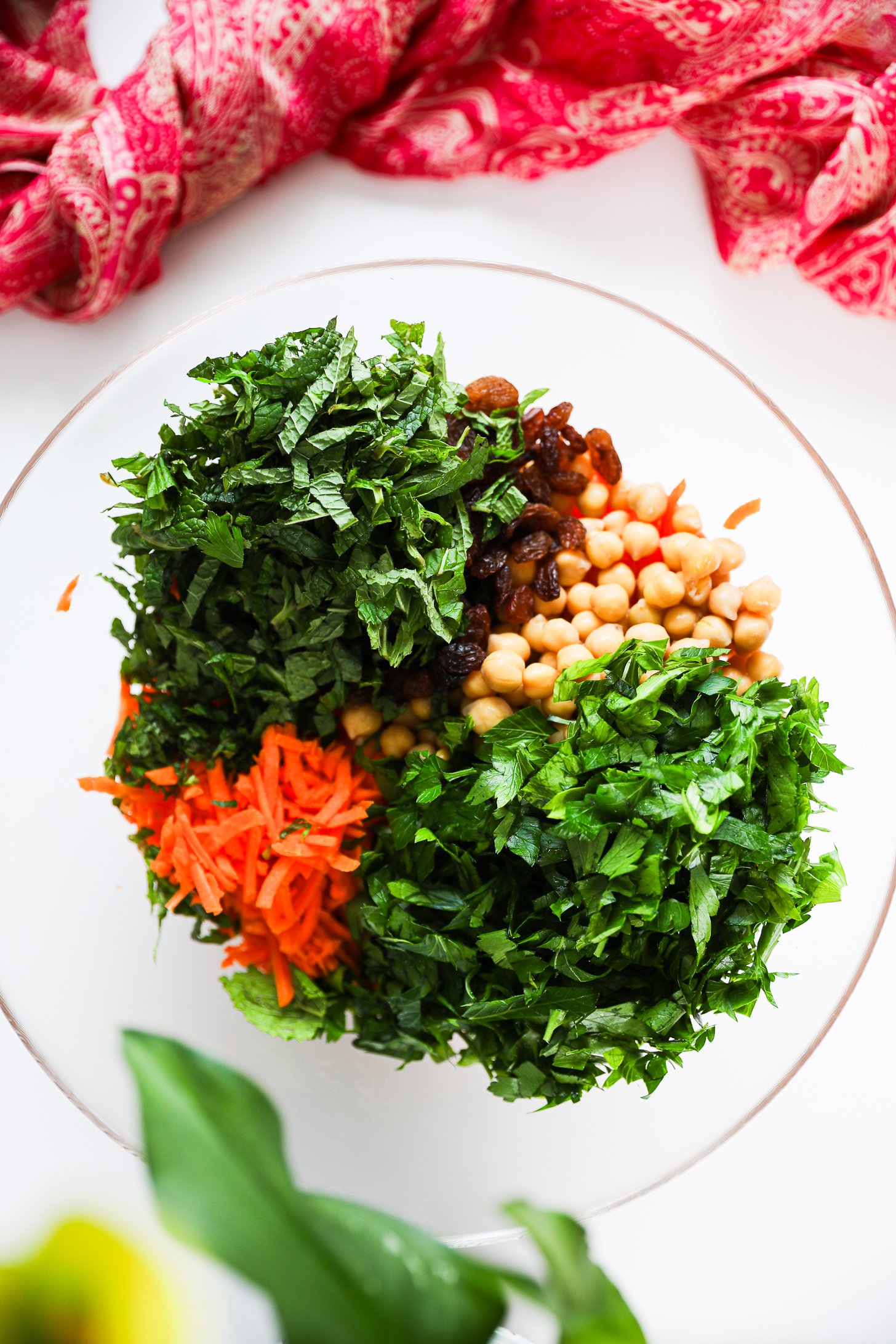 Overhead view of a salad bowl with grated carrots, chickpeas, raisins and herbs side by side.