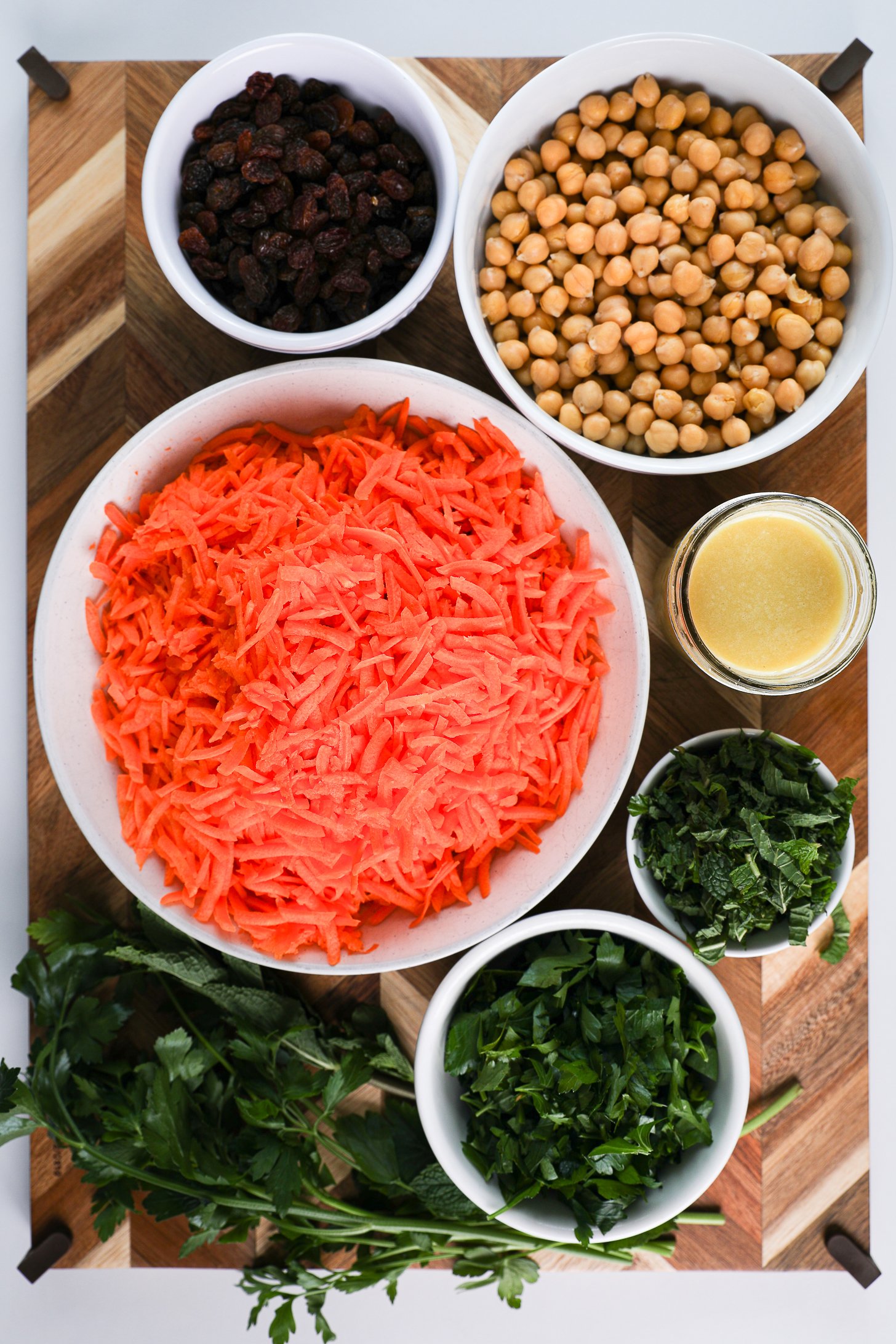 A selection of food ingredients like grated carrots, chickpeas, raisins, fresh herbs and dressing.