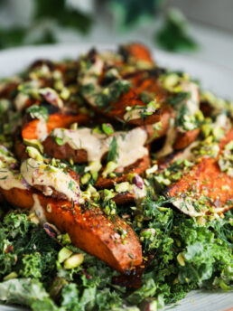 A perspective image of kale topped with spicy roasted sweet potato wedges covered in a creamy dressing and chopped pistachios.