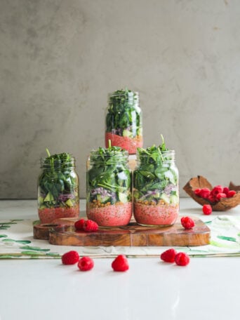 A vibrant styled display of four layered mason jar spring salads with raspberries all around.