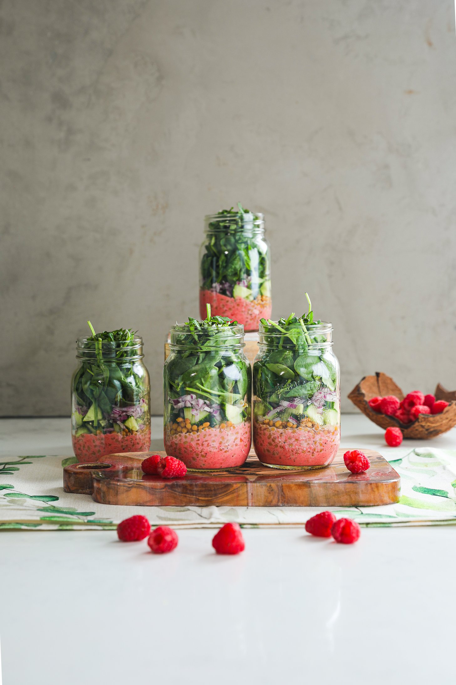 A vibrant styled display of four layered mason jar spring salads with raspberries all around.