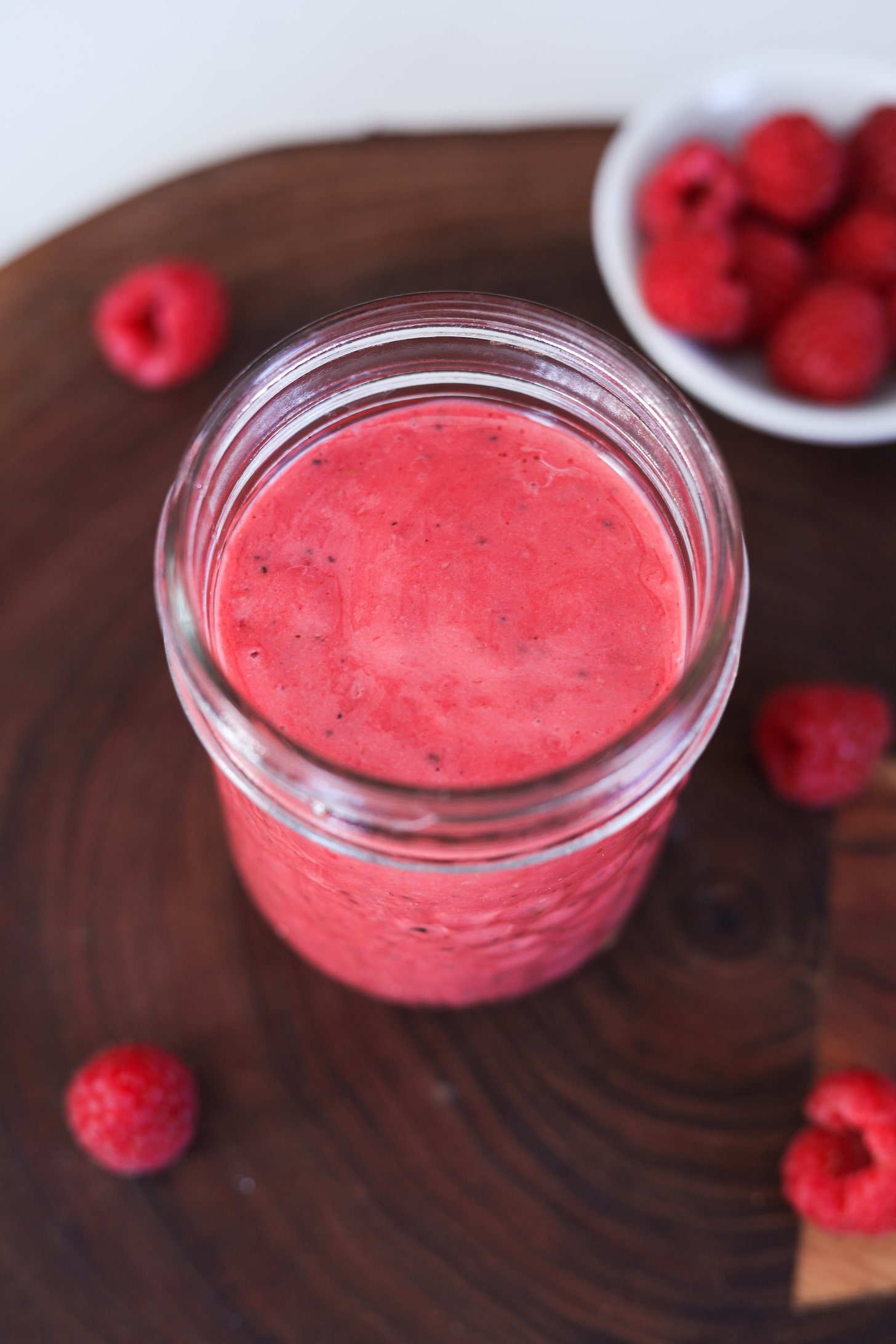 Image of a mason jar of vibrant raspberry dressing with fresh raspberries in the back- and foreground.