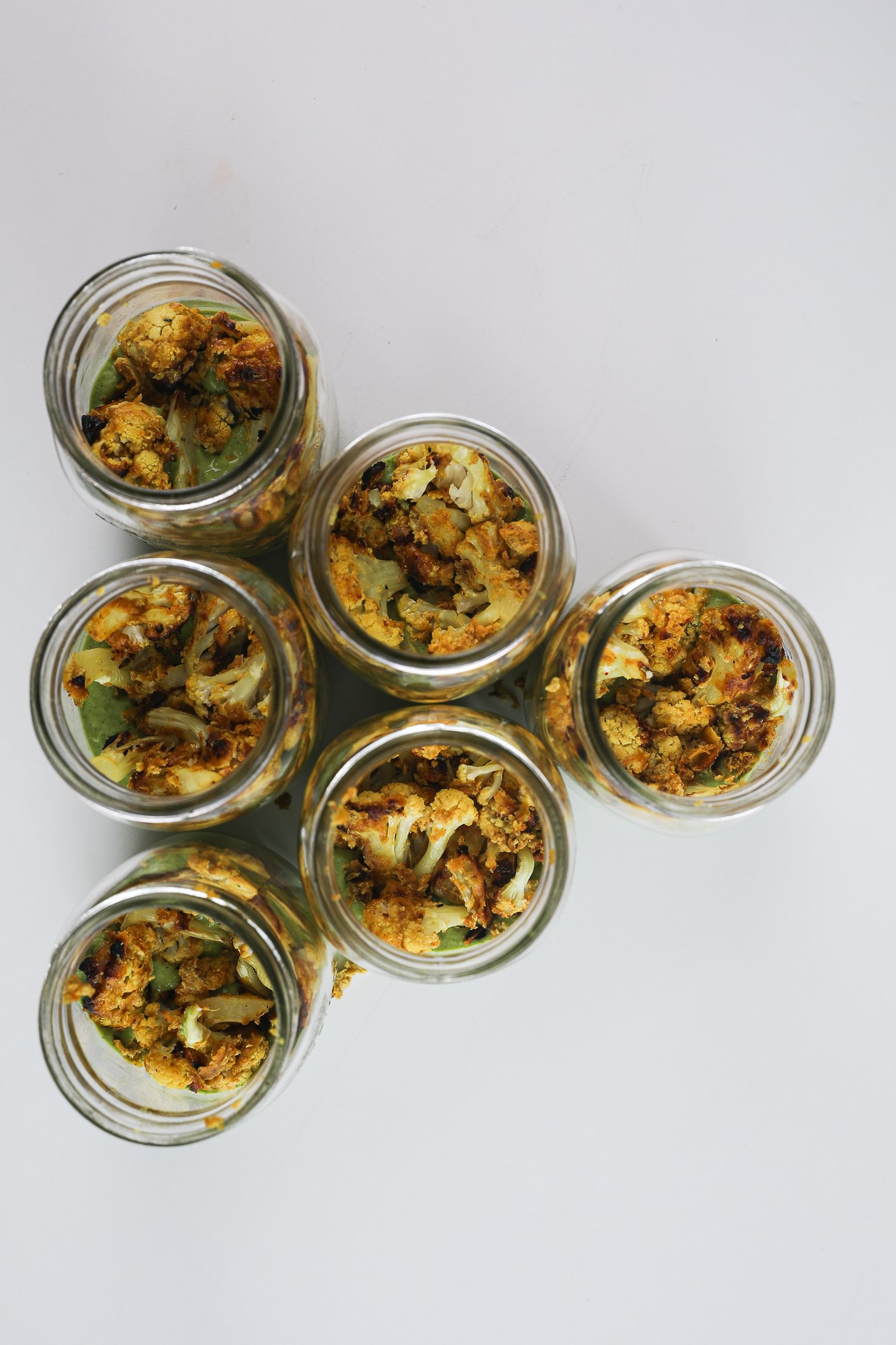 Six mason jars with avocado cilantro lime dressing at the base topped with a second layer of tandoori cauliflower.