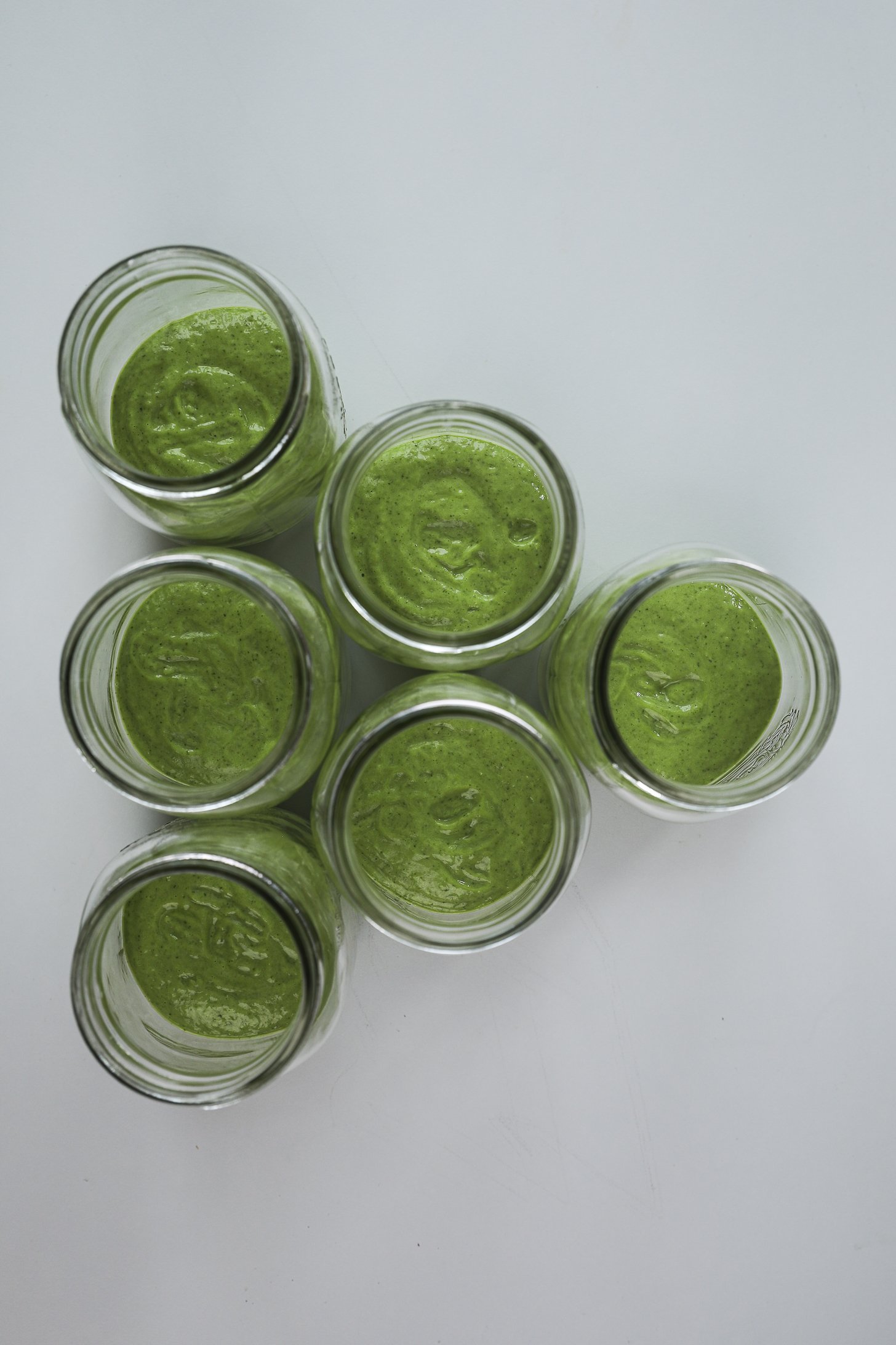Six mason jars with avocado cilantro lime dressing at the base.