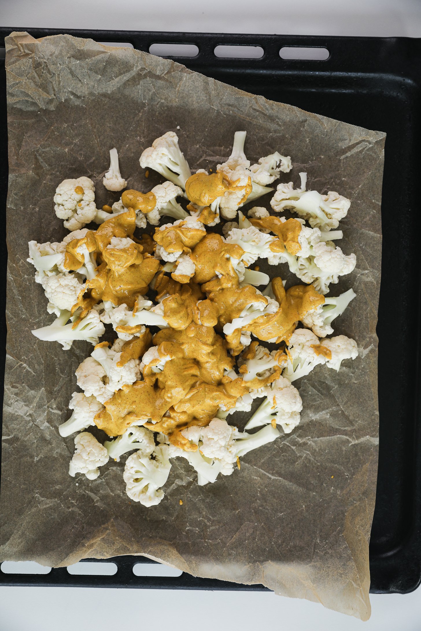 Overhead image of cauliflower florets topped with creamy tandoori marinade on a lined baking tray.