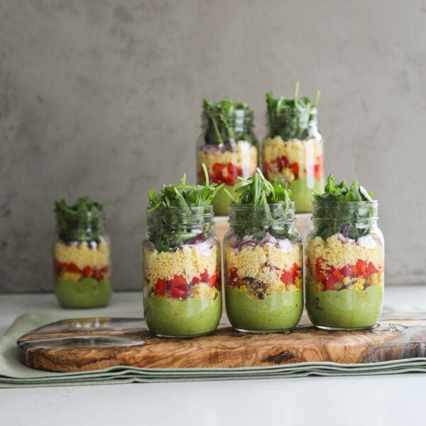 Face on image of six coloufully layered mason jar salads styled against a grey back drop.