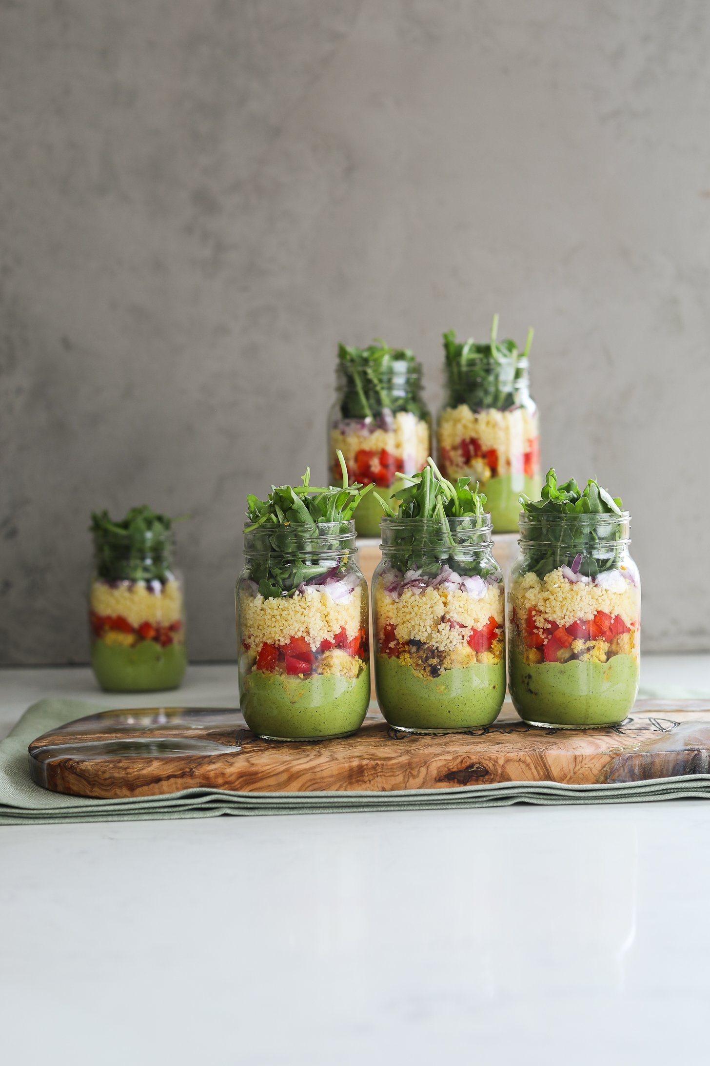 Face on image of six coloufully layered mason jar salads styled against a grey back drop.