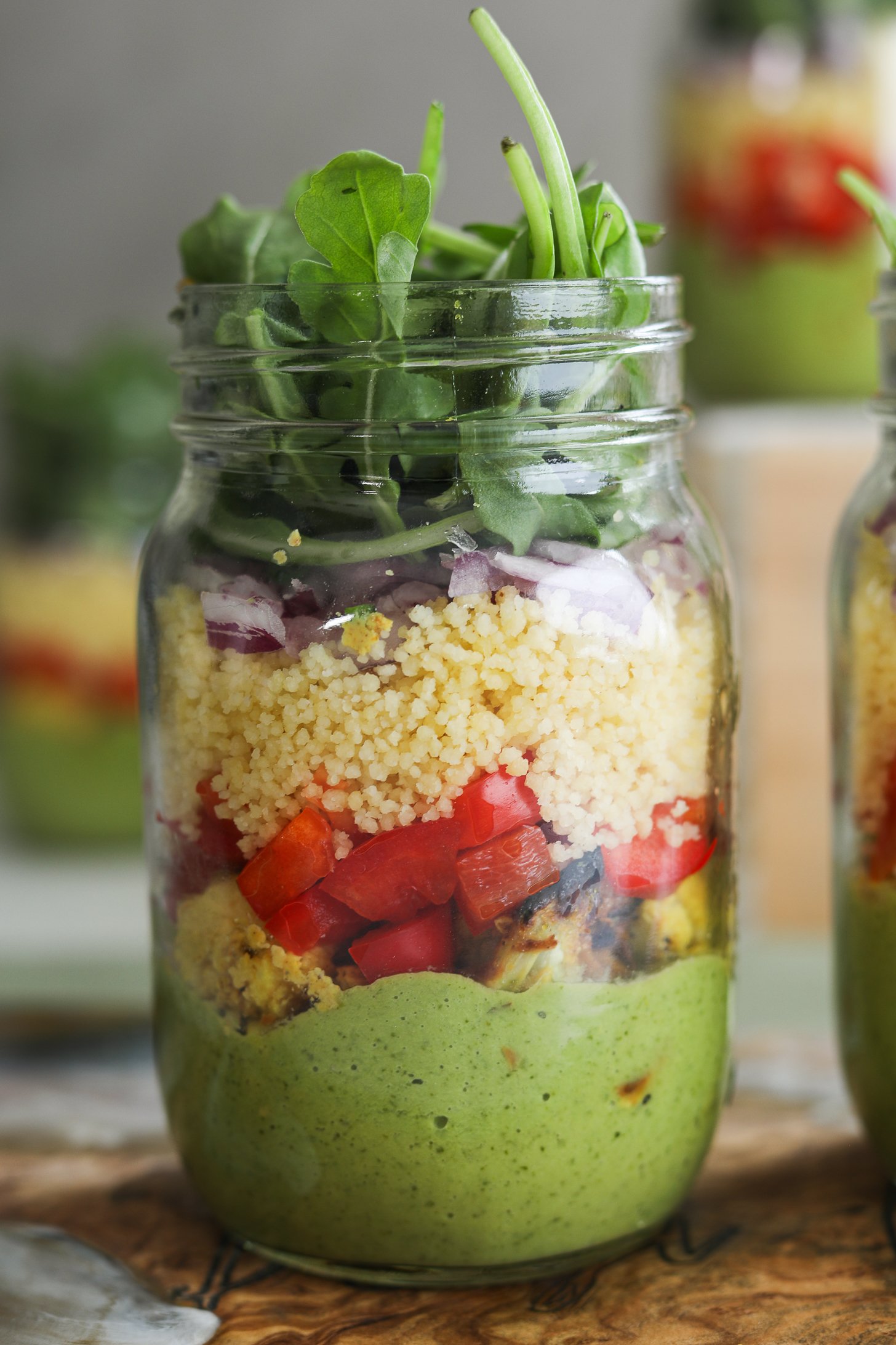 Face on image of a layered mason jar salad with arugula protruding out.