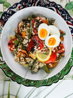 Top view image of a bowl of barley salad with mixed grilled veggie topped with boiled egg halves.