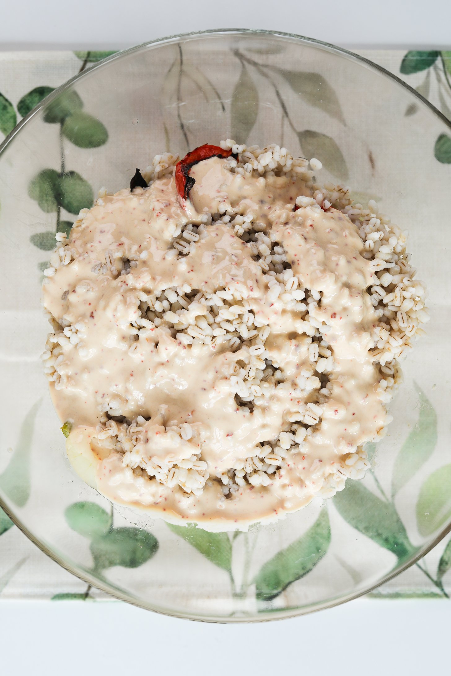Top view of a bowl of cooked barley topped with a white creamy tahini dressing.