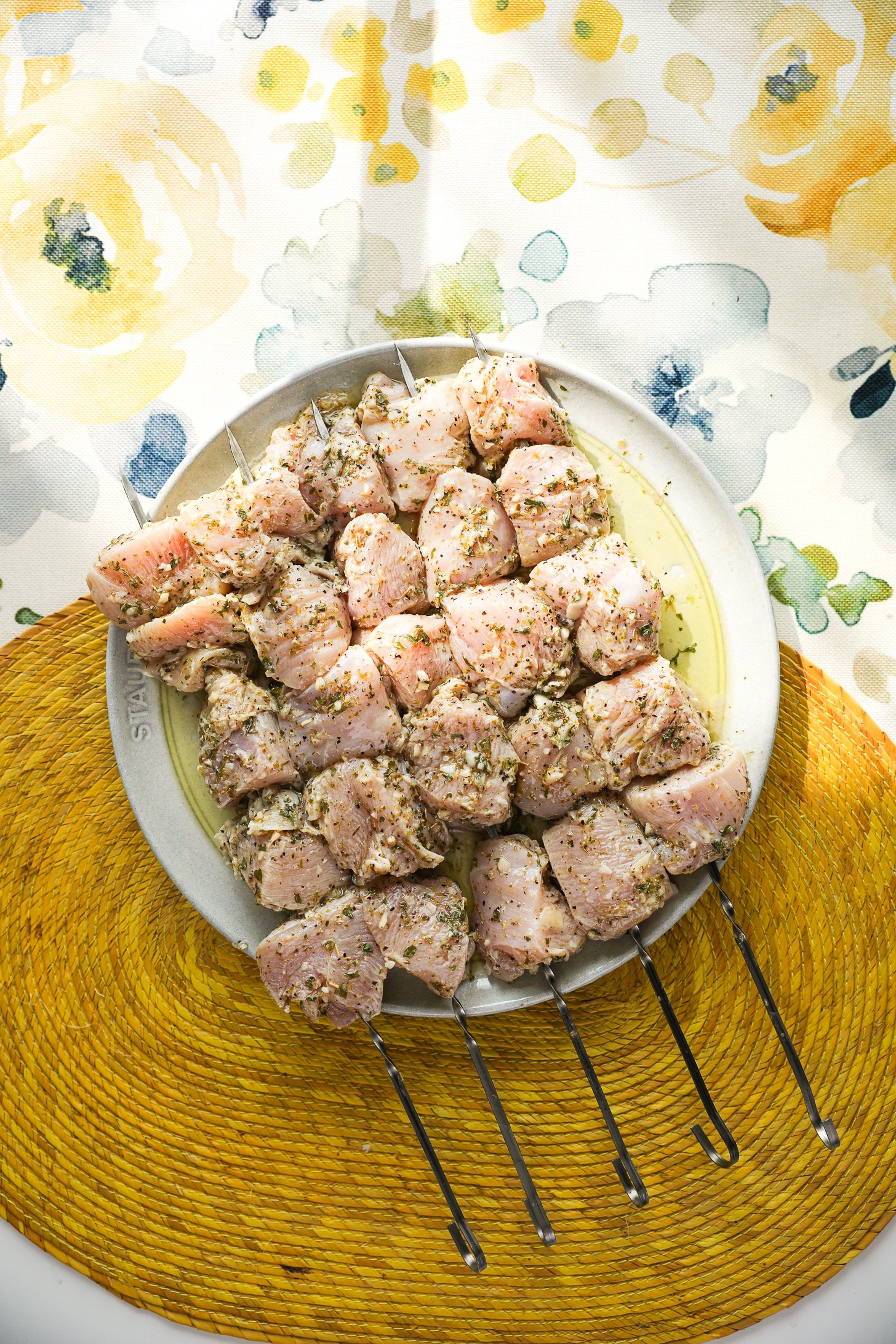 Skewers of marinated raw chicken breast on a plate.