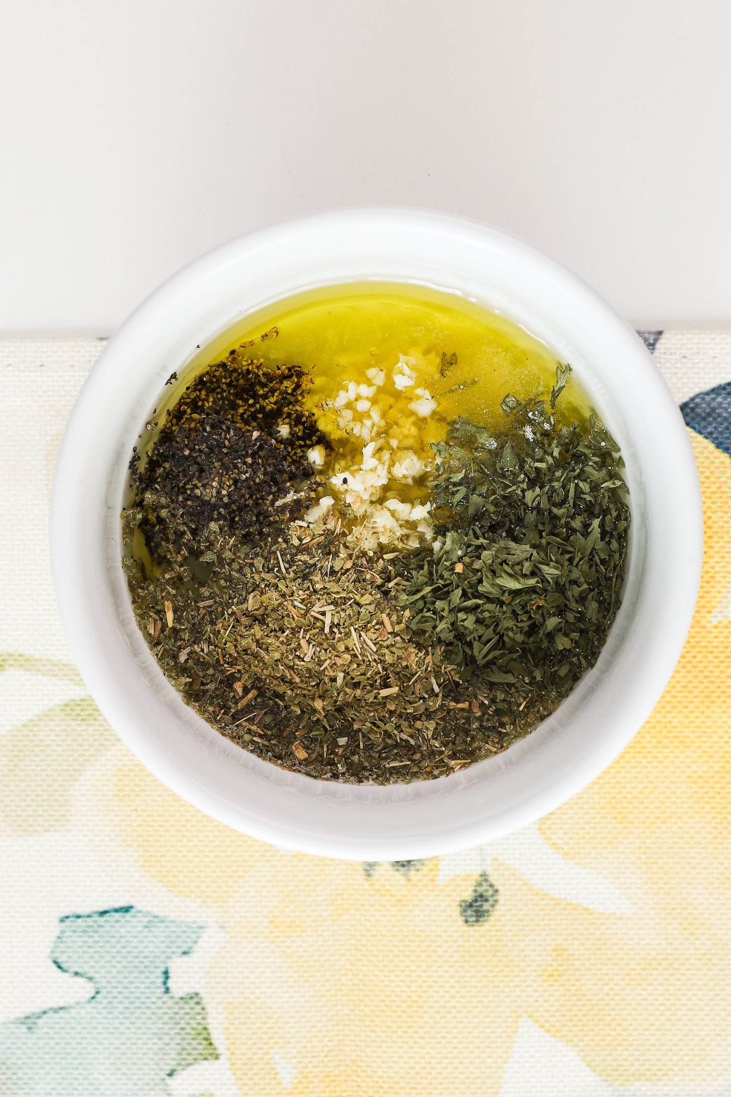 A bowl with oil with crushed garlic topped with dried herbs and black pepper.