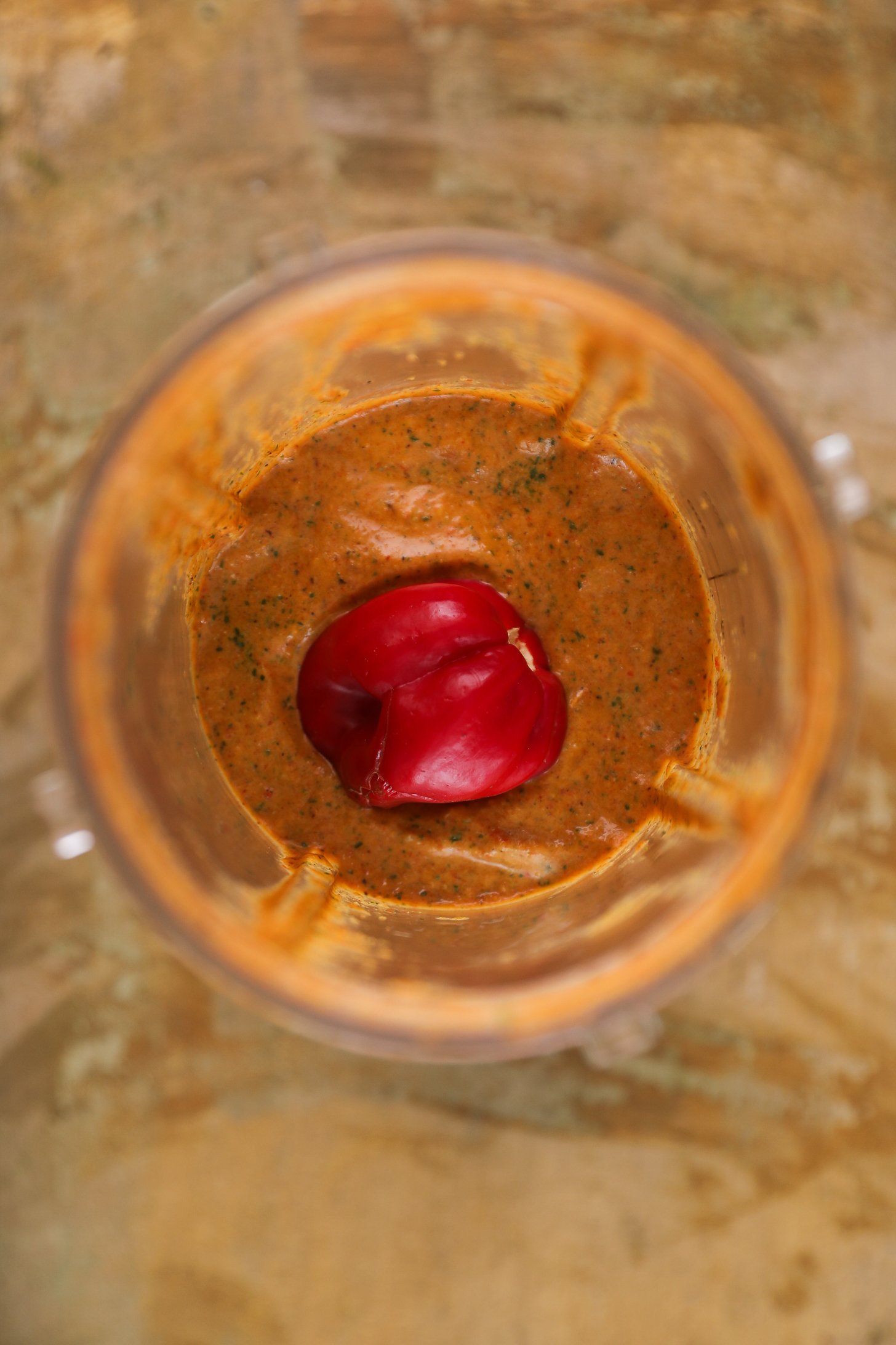 Top view of blender cup half full with a thick orange coloured marinade with a red habanero chilli pepper on top.