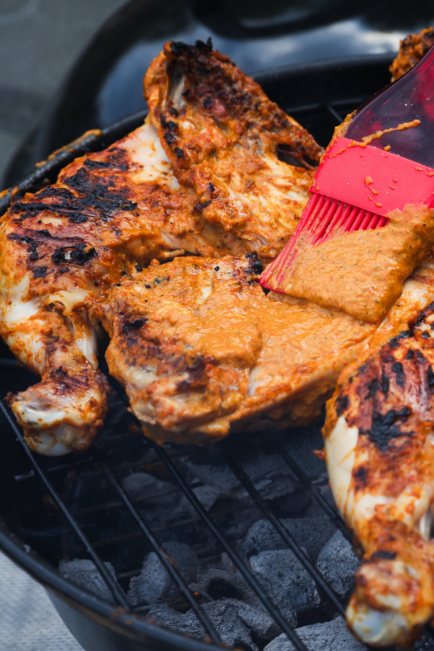 Brush basting marinade on the bottom side of a chicken leg and thigh on a charcoal grill.