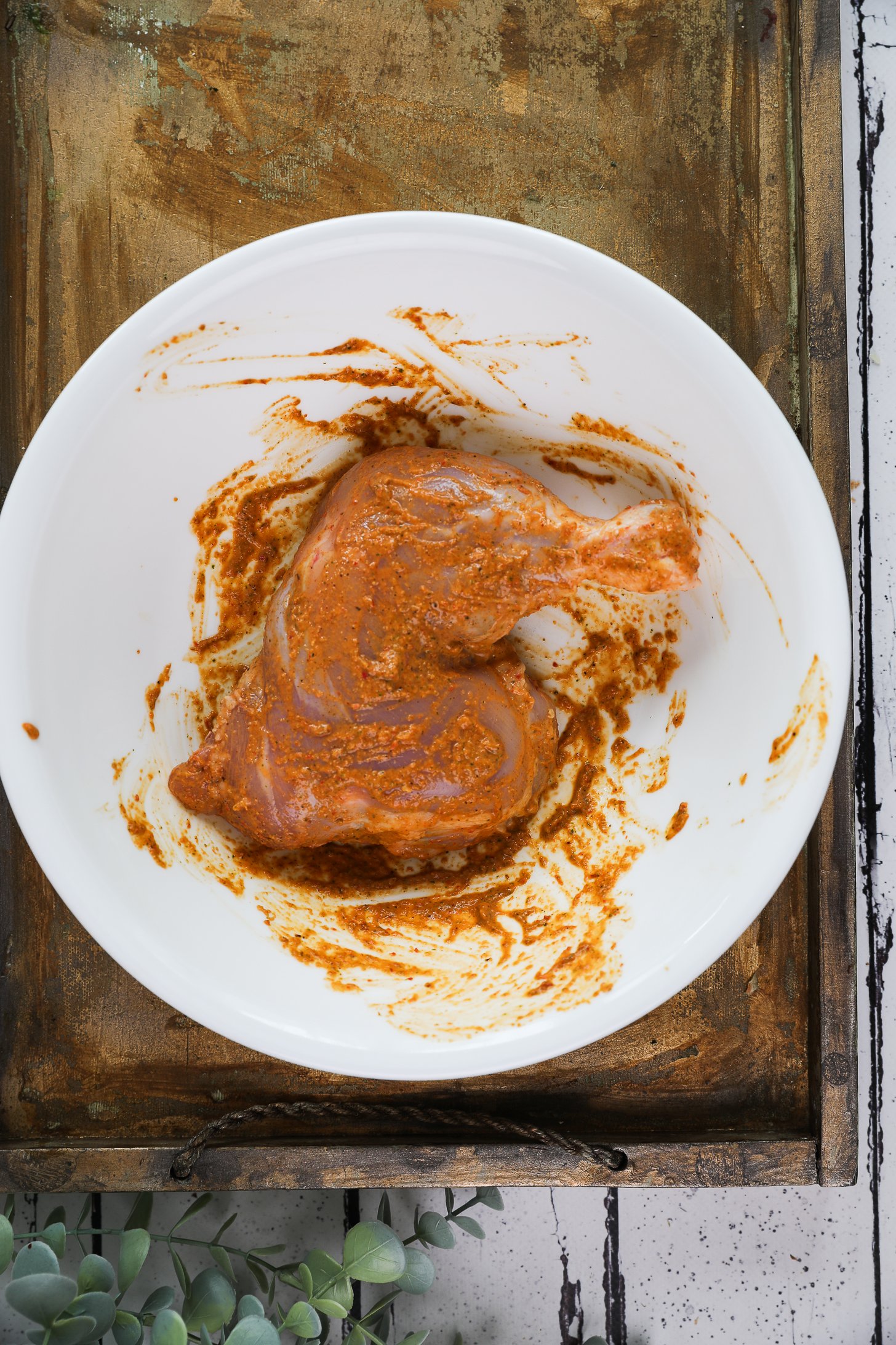 One leg thigh coated in an orange marinade in a large bowl.