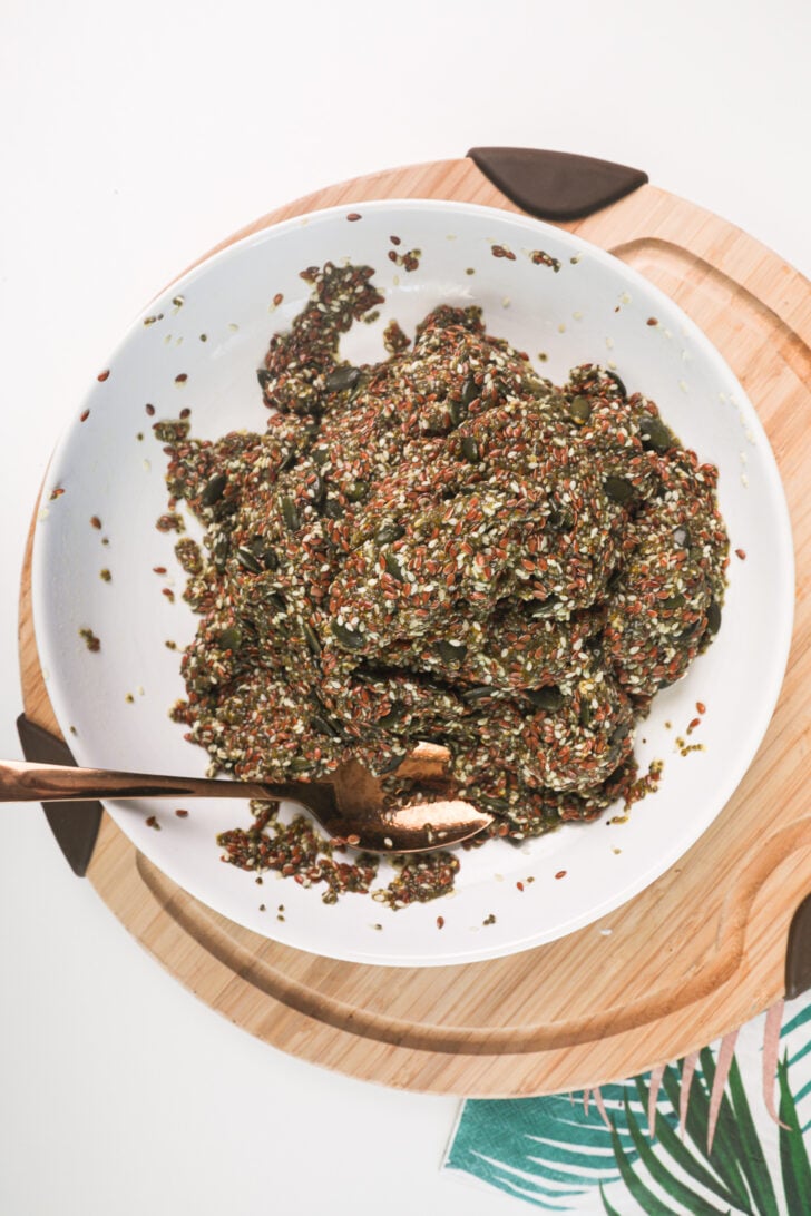 A bowl of mixed seeds and water, forming a thick dough-like consistency, with a spoon resting inside.