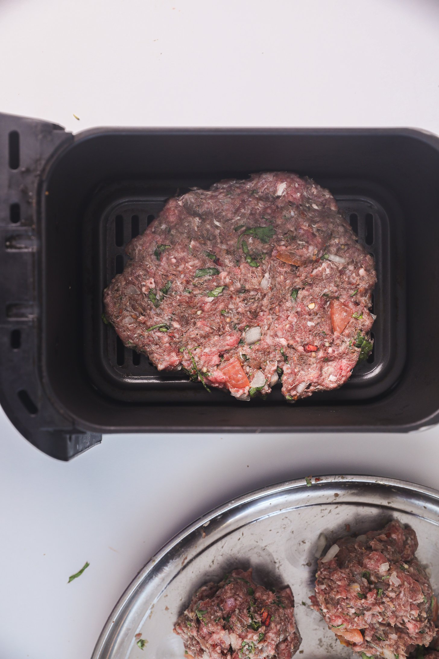 A raw Chapli Kebab patty placed in an air fryer basket, with additional raw kebab balls on a tray nearby.