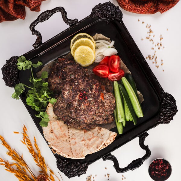 Chapli Kebabs served on a tray with naan, cucumber slices, tomatoes, lemon slices, and coriander, with decorative elements around the tray.