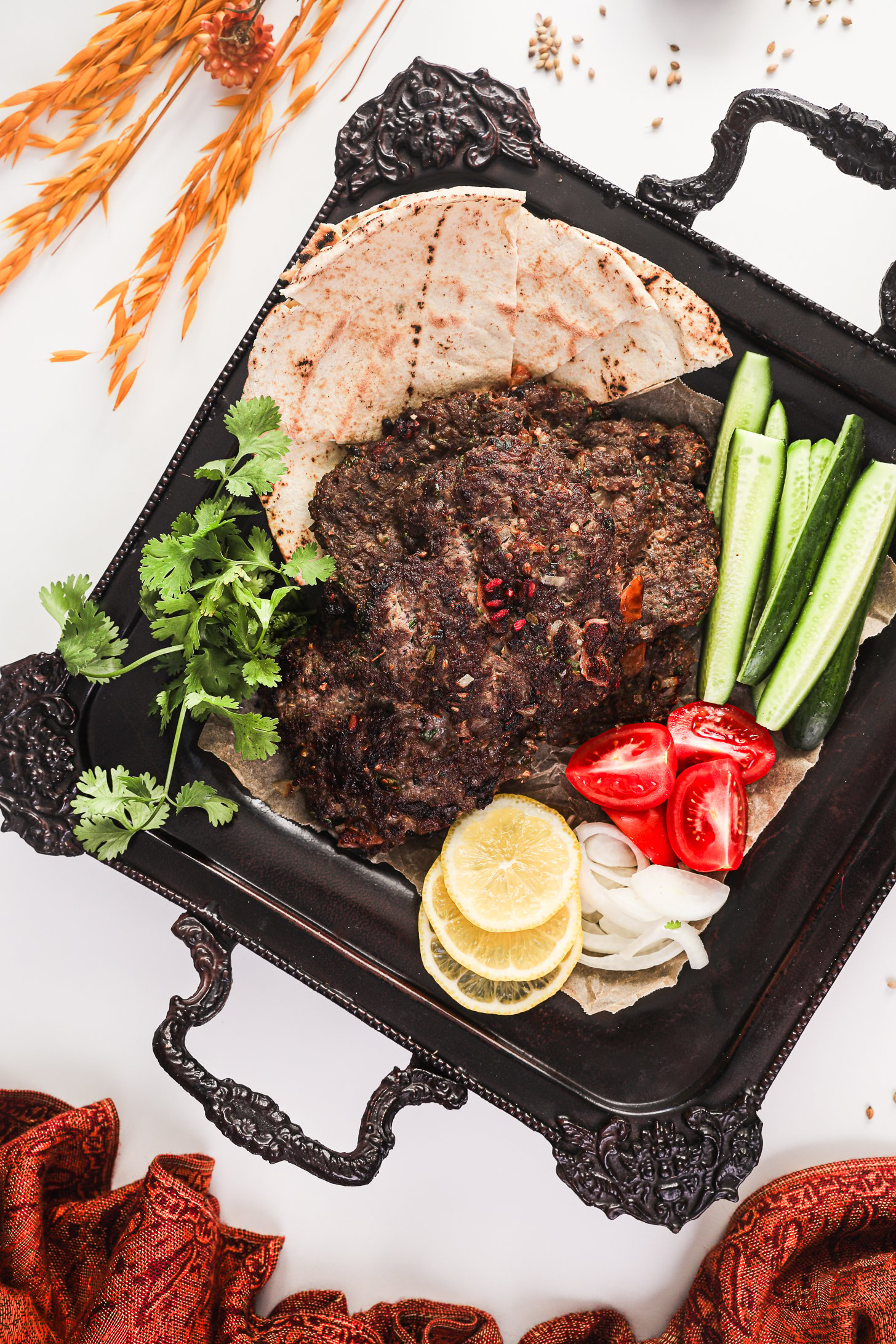 Chapli Kebabs served on a tray with naan, cucumber slices, tomatoes, lemon slices, and coriander.