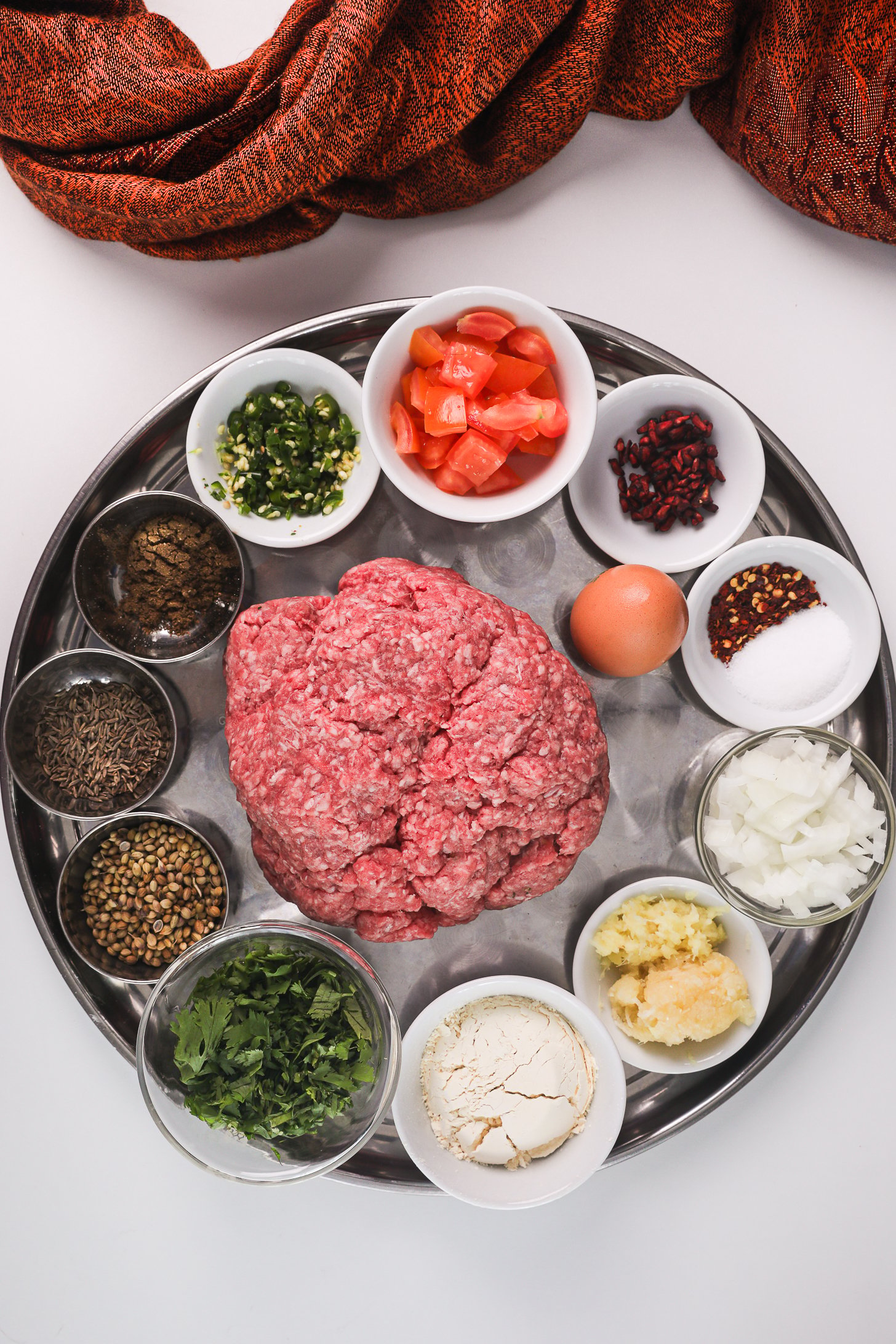 Ingredients for Chapli Kebabs including ground meat, chopped vegetables, and spices on a tray.