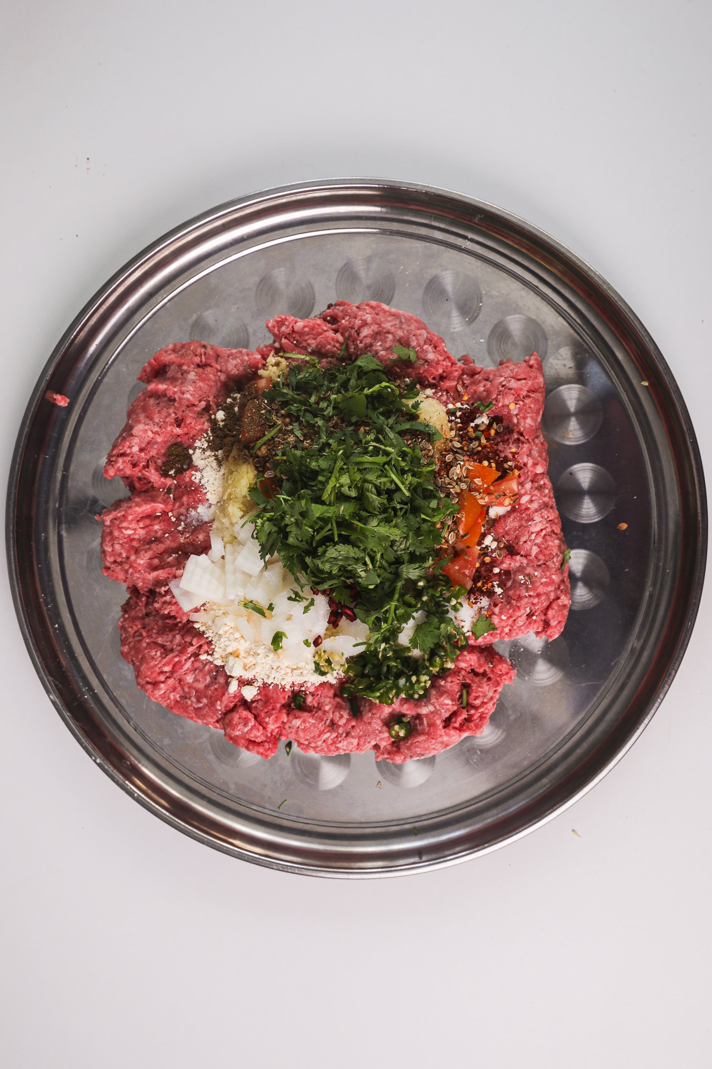 Ground meat with chopped onions, tomatoes, coriander, and spices in a tray.