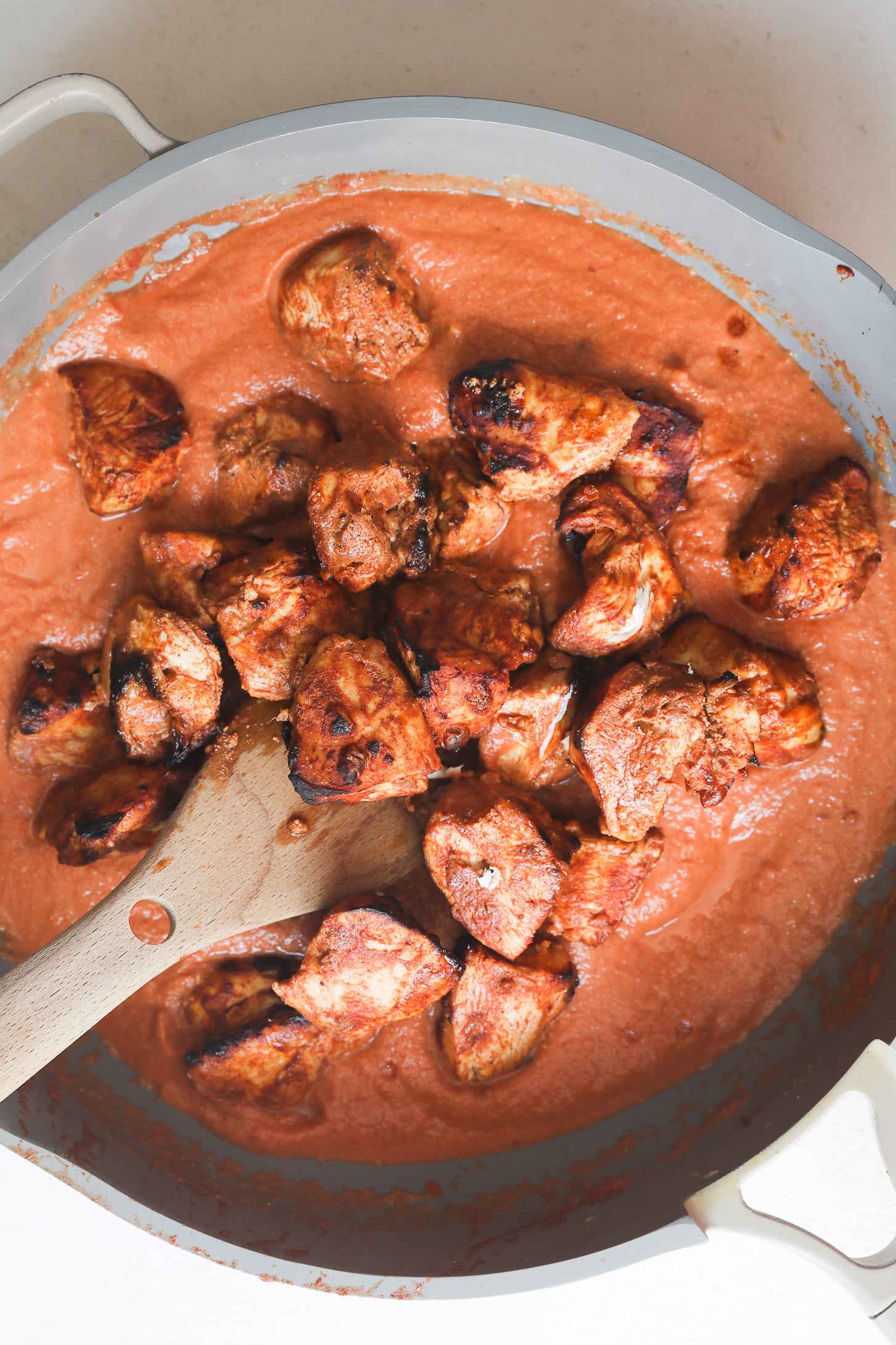 Des morceaux de poitrine de poulet grillés au charbon de bois sont mélangés à du masala de tomates lisses dans une poêle à frire grise.