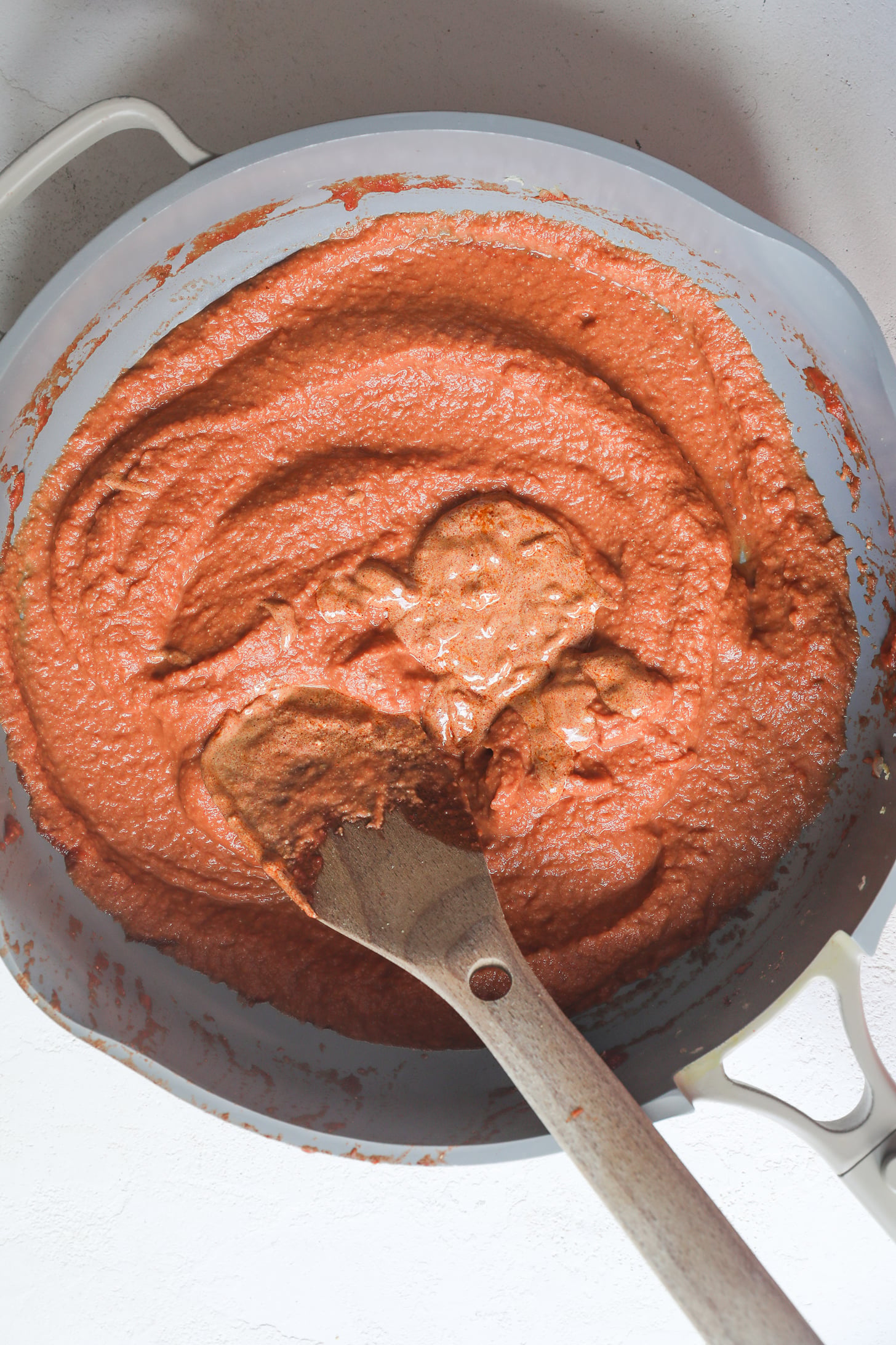 Sauce tomate mélangée lisse dans une poêle grise avec une cuillère en bois.