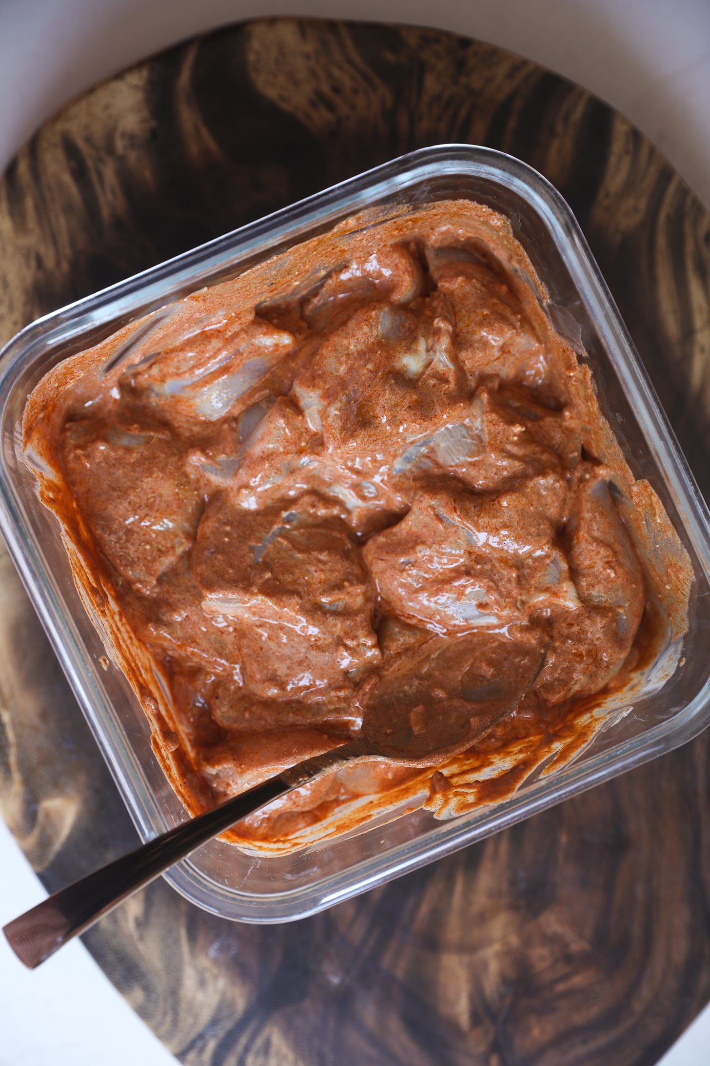 Morceaux de poitrine de poulet crus recouverts de sauce au yaourt rouge épicée dans un bol en verre.