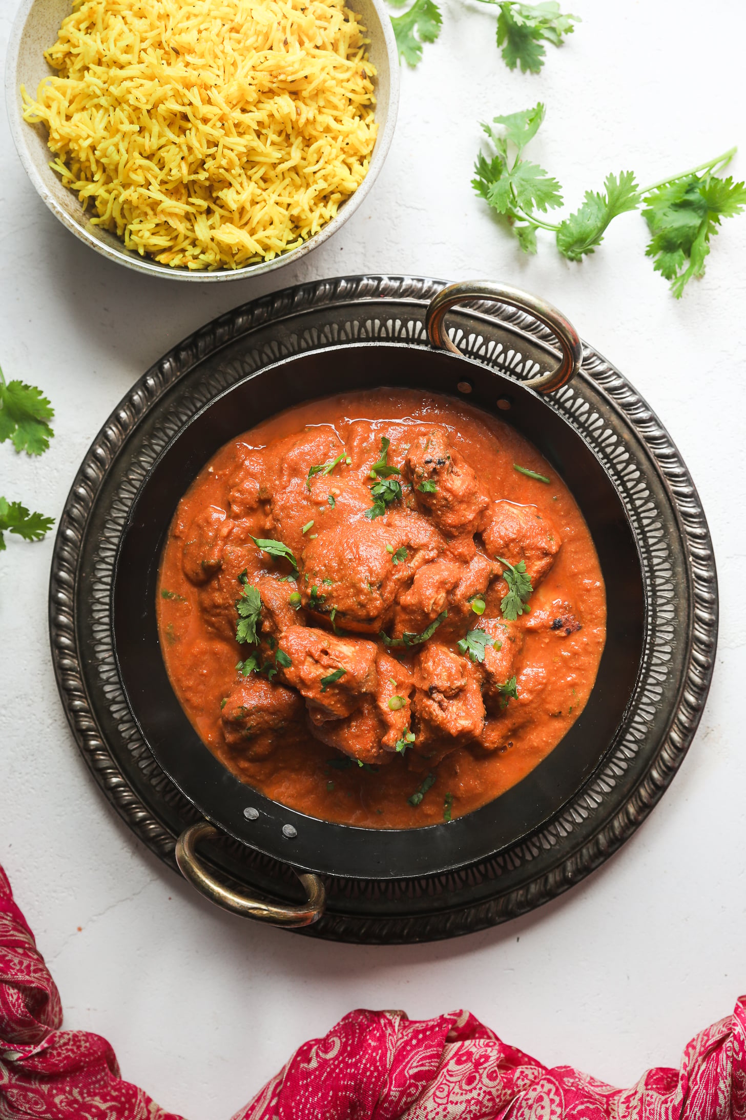 Vue aérienne d'un poulet au curry dans un plat de service noir avec un bol de riz jaune à proximité.