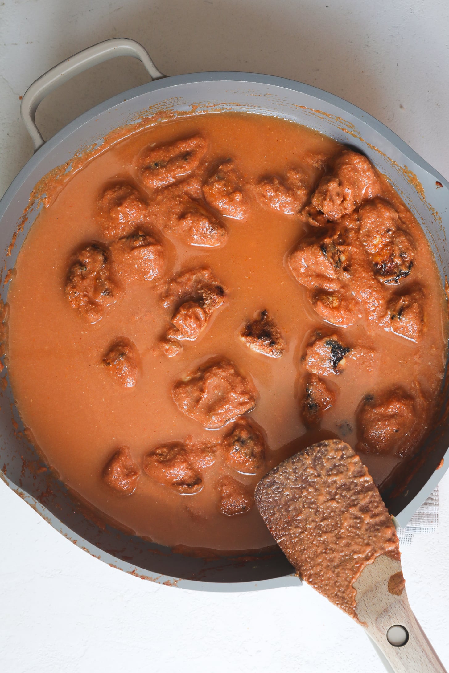 Morceaux de poitrine de poulet grillés dans une sauce tomate aqueuse dans une poêle grise.