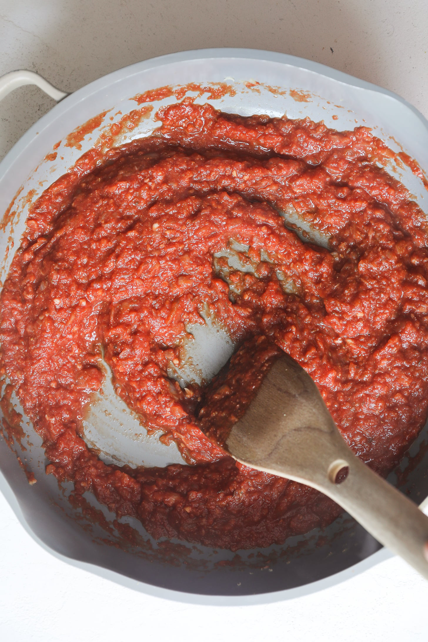 Mélange de tomates épais et grumeleux dans une poêle grise avec une cuillère en bois.