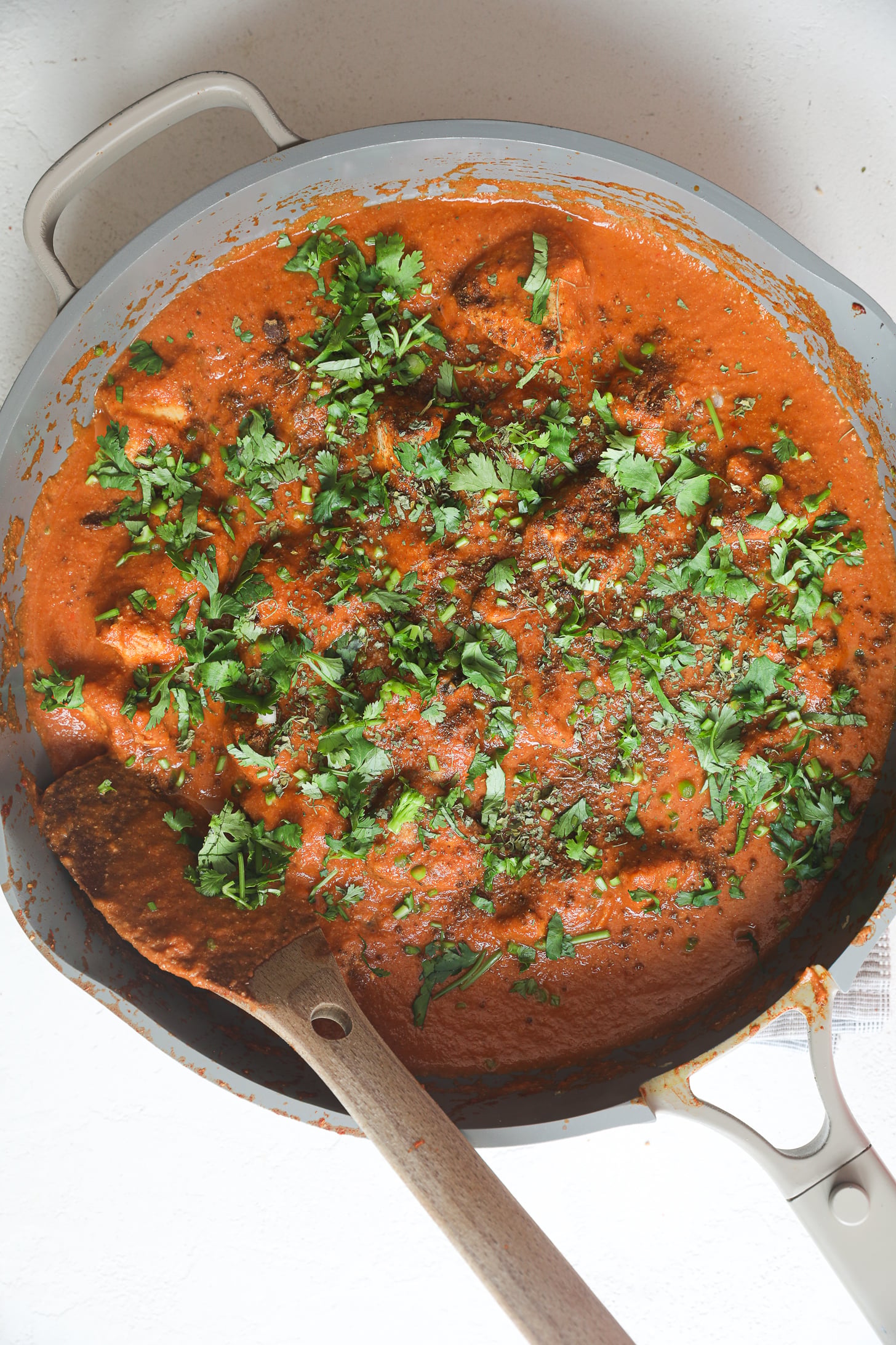 Une grande poêle grise remplie de tomates au curry et garnie de coriandre hachée et d'épices moulues.
