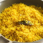 Close up of yellow rice topped with a bay leaf in a pan.