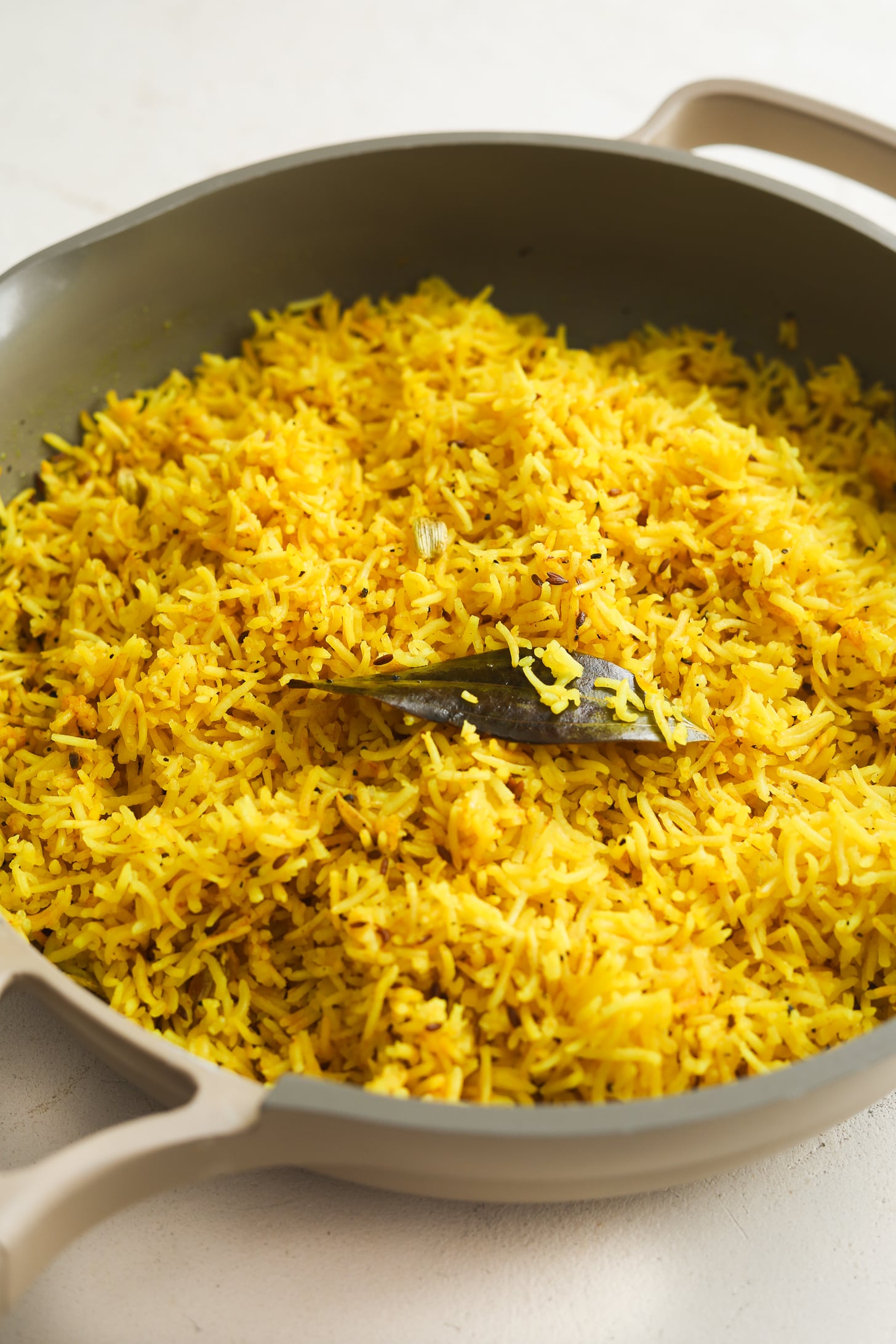 Riz au curcuma indien sur la cuisinière (si facile !) 12 Gros plan de riz jaune recouvert de feuille de laurier dans une poêle.